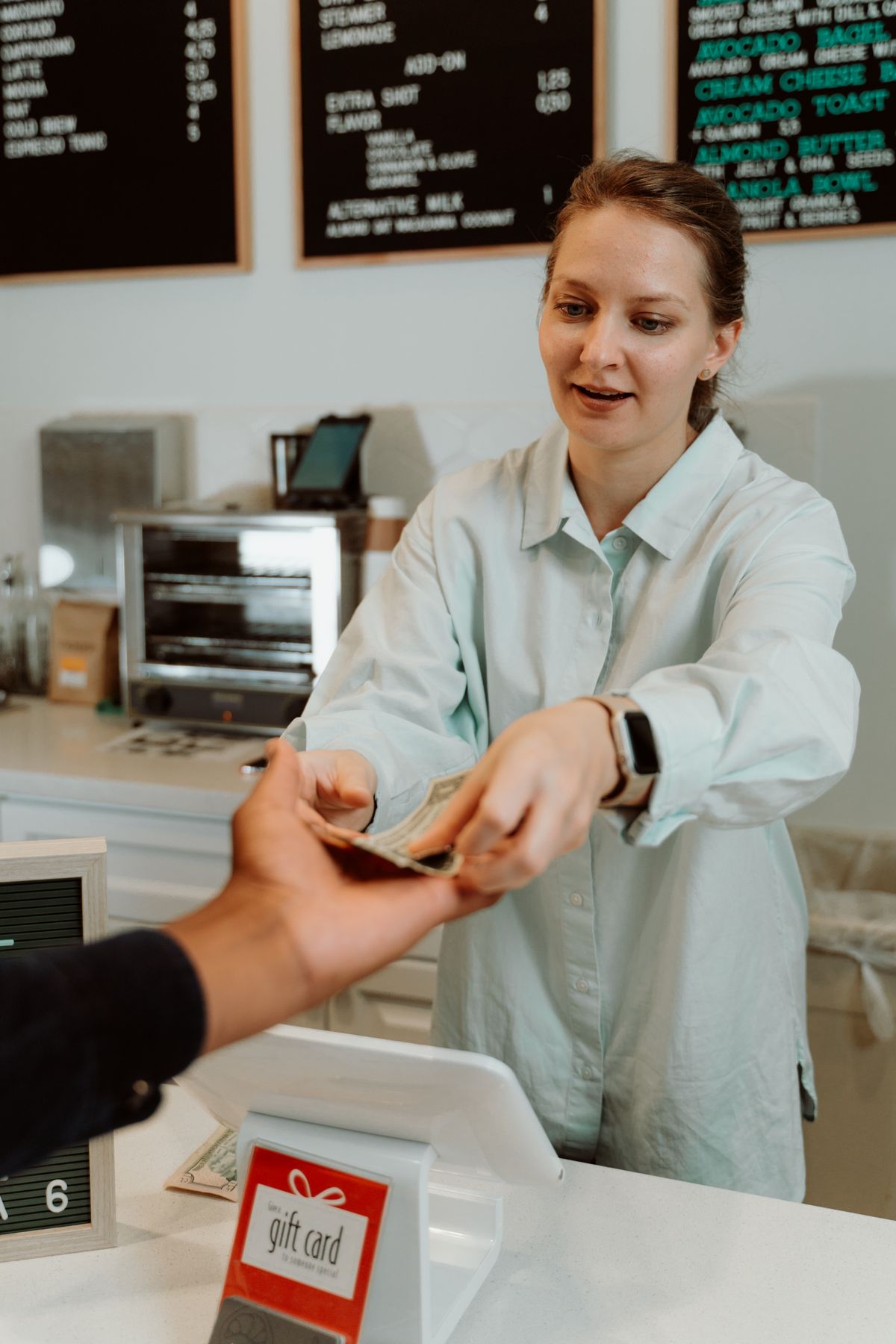 A café worker taking payment at the counter, with a gift-card display on the till