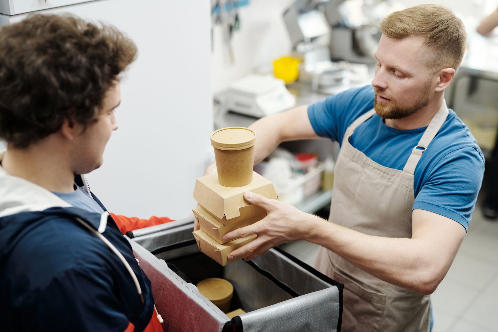 A restaurant worker handing a packed delivery order to a courier with an insulated bag
