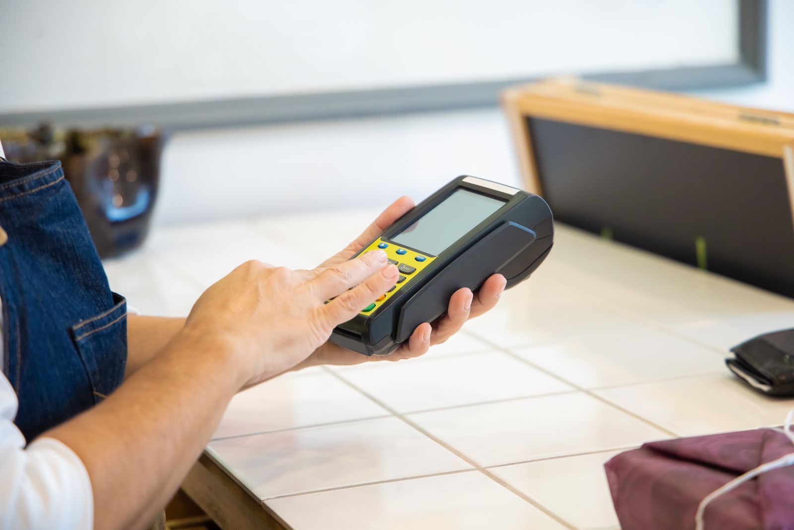 A hand holding a card payment terminal at a café counter